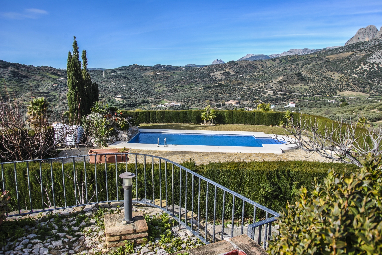 Vista de la piscina y el paisaje desde la era de Cortijo Las Monjas. Alojamiento turístico e histórico de la provincia de Málaga, en la Alta Axarquía, Andalucía. Montañas de Alfarnatejo y Periana