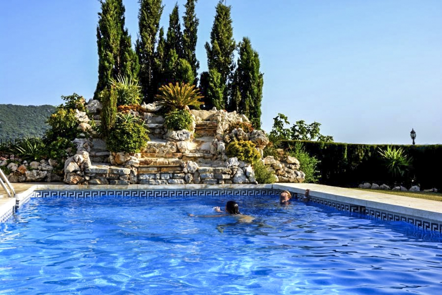 Cascada y piscina del alojamiento turístico e histórico Cortijo Las Monjas. Huéspedes disfrutando de un soleado día en el interior de la Costa del Sol, Axarquía de Málaga. Andalucía